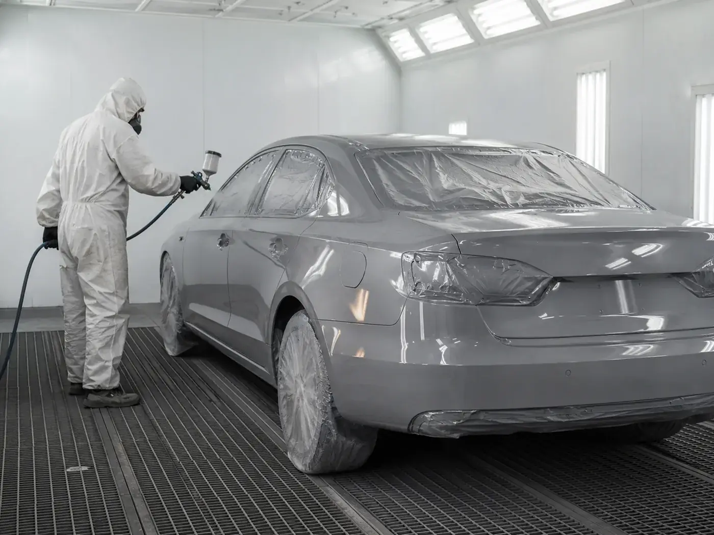 Carro dentro de cabine de pintura clara recebendo aplicação de tinta, com acabamento uniforme.